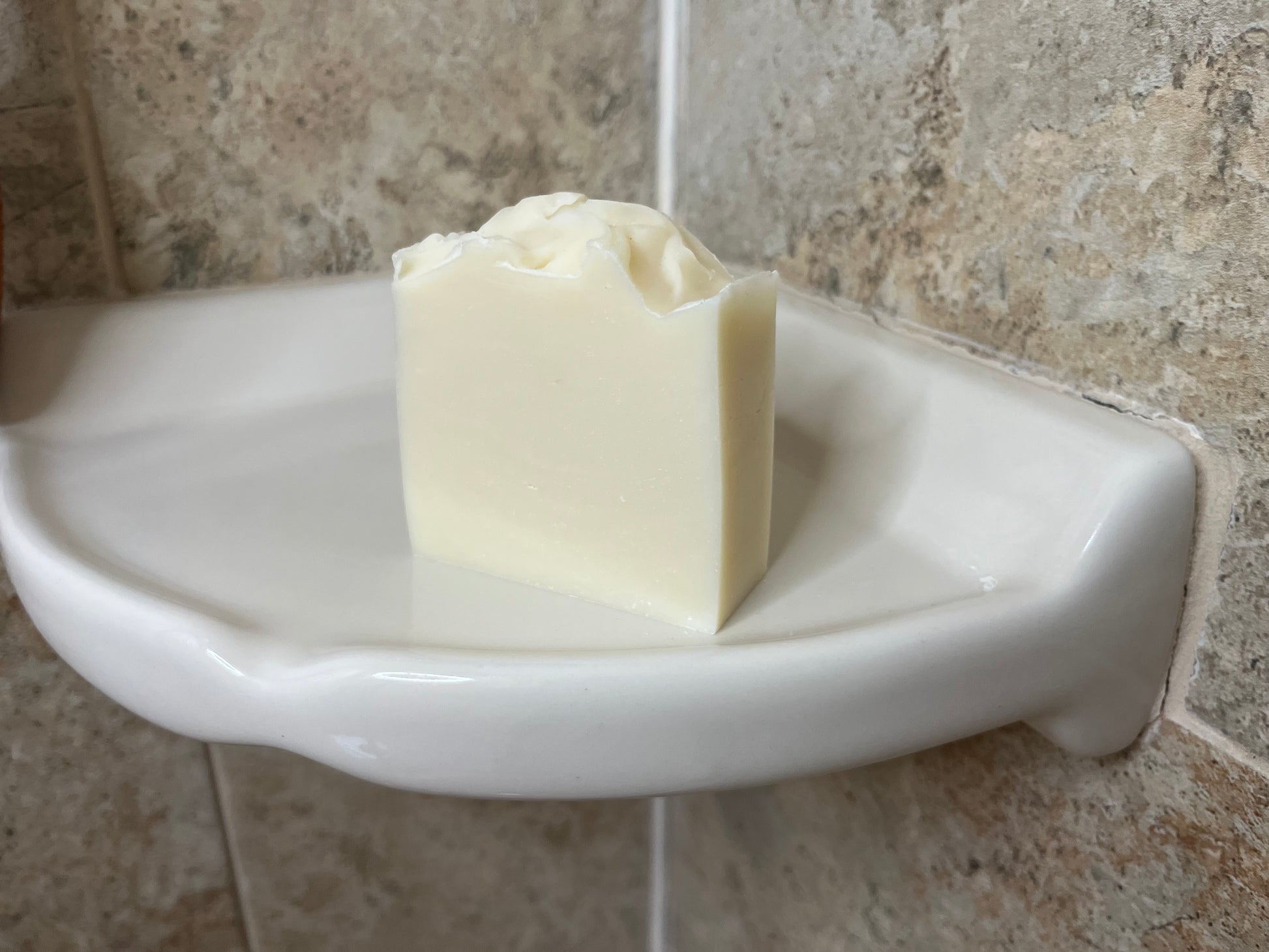 Unlabelled vegan soap on a white soap dish against a tiled bathroom wall.